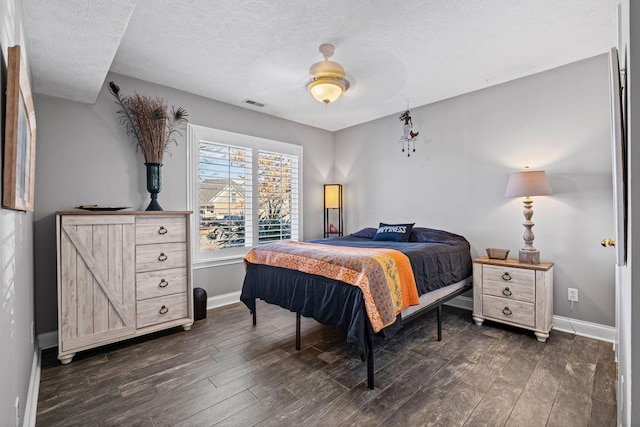 bedroom with visible vents, dark wood finished floors, a textured ceiling, and baseboards