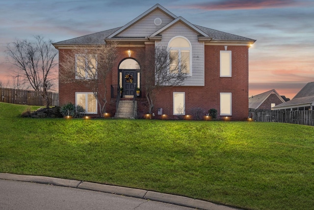 view of front of house with brick siding, a yard, and fence