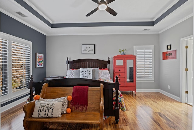 bedroom featuring a tray ceiling, wood finished floors, visible vents, and crown molding