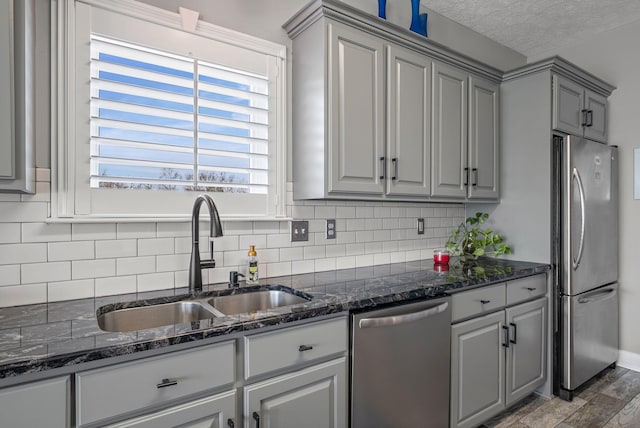 kitchen featuring decorative backsplash, dark stone counters, appliances with stainless steel finishes, gray cabinets, and a sink