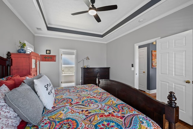 bedroom featuring visible vents, wood finished floors, ensuite bathroom, a tray ceiling, and crown molding