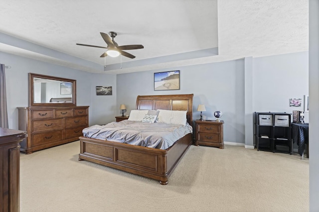 bedroom featuring a tray ceiling, light carpet, ceiling fan, and baseboards