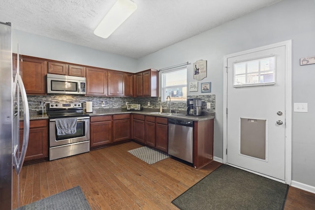 kitchen featuring stainless steel appliances, a sink, decorative backsplash, and dark wood-style floors