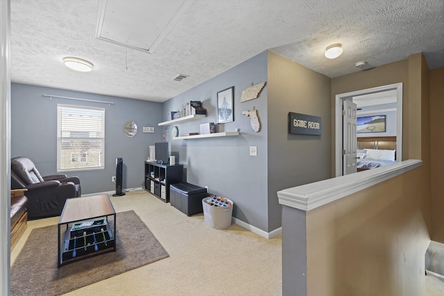 interior space featuring a textured ceiling, visible vents, baseboards, carpet, and attic access