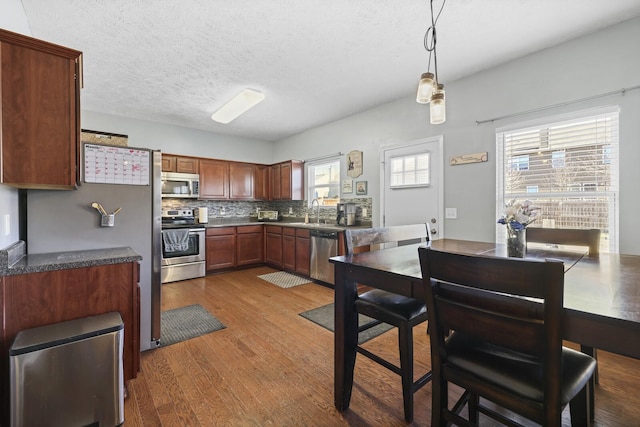 kitchen featuring backsplash, wood finished floors, stainless steel appliances, a textured ceiling, and a sink