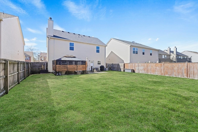 rear view of property with a fenced backyard, a yard, a chimney, and a gazebo