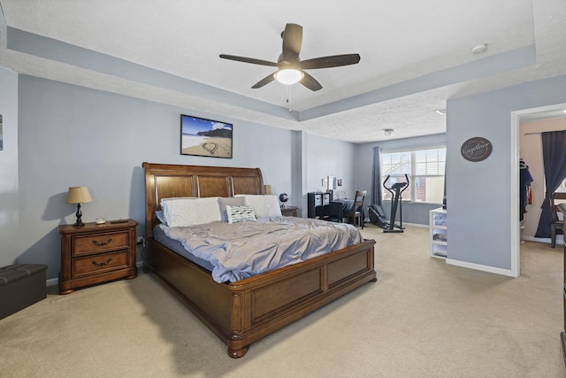 bedroom featuring baseboards, a ceiling fan, light colored carpet, a tray ceiling, and a textured ceiling