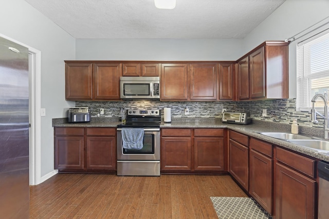 kitchen with decorative backsplash, dark countertops, dark wood-style floors, stainless steel appliances, and a sink