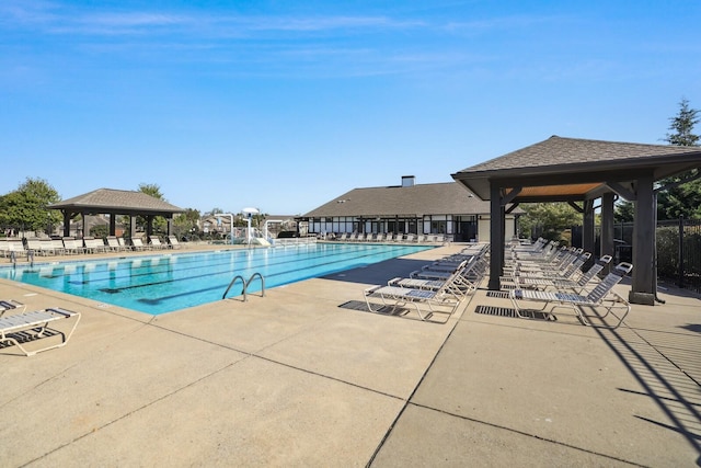 community pool with a patio, fence, a water slide, and a gazebo