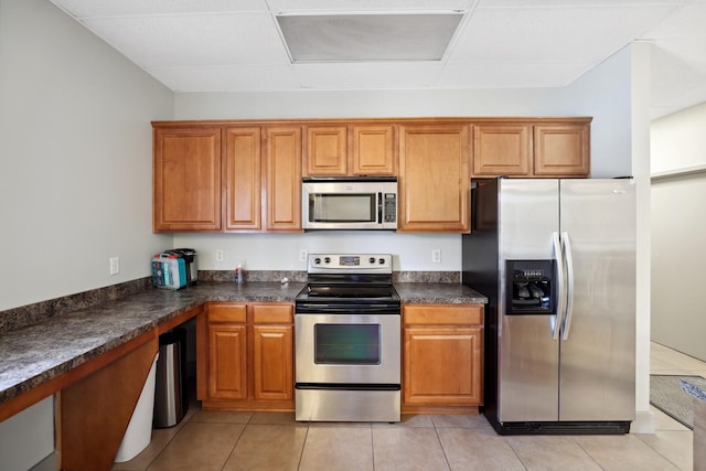 kitchen with dark countertops, light tile patterned floors, appliances with stainless steel finishes, and brown cabinetry