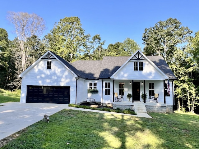 view of front of property with an attached garage, covered porch, driveway, roof with shingles, and a front yard