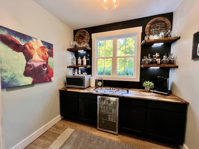 bar featuring a dry bar, stainless steel microwave, light wood-style flooring, white gas cooktop, and beverage cooler