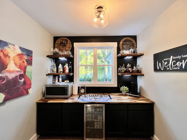 bar with gas stovetop, stainless steel microwave, a bar, beverage cooler, and baseboards