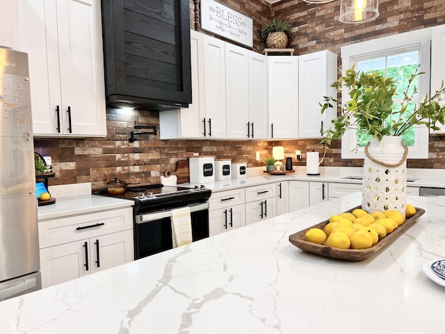 kitchen with electric stove, light stone countertops, freestanding refrigerator, and white cabinets