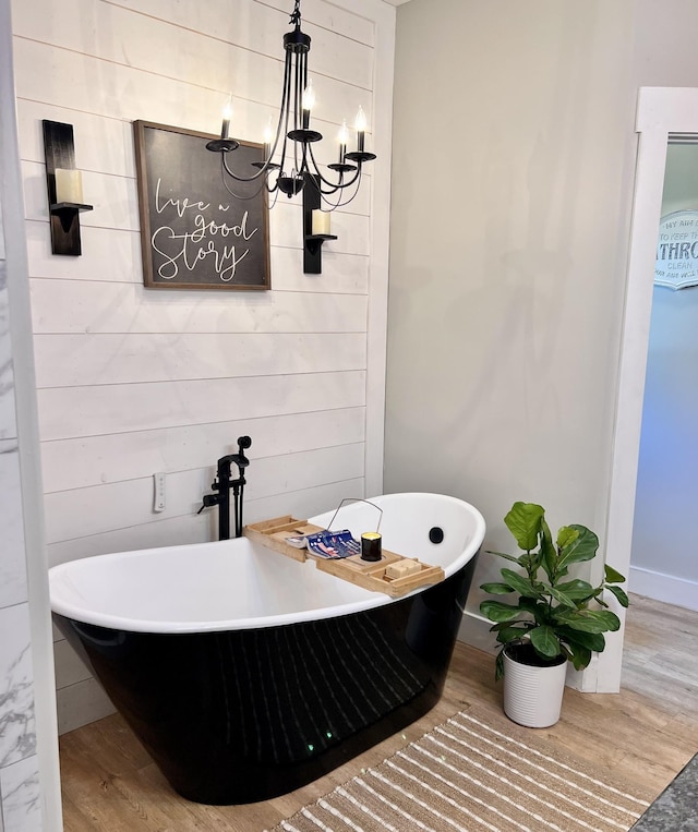 bathroom with a soaking tub, a chandelier, wood finished floors, and wood walls