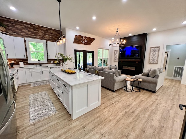 kitchen with a chandelier, a kitchen island, a sink, visible vents, and open floor plan