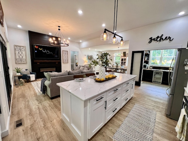 kitchen featuring visible vents, a chandelier, freestanding refrigerator, a fireplace, and white cabinetry