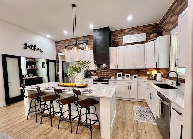 kitchen featuring white cabinets, light wood-style flooring, a kitchen island, appliances with stainless steel finishes, and a sink