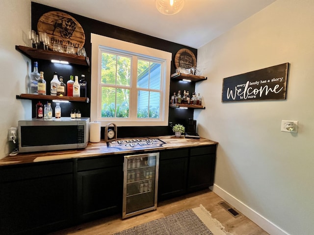 bar featuring wine cooler, stainless steel microwave, visible vents, a bar, and baseboards