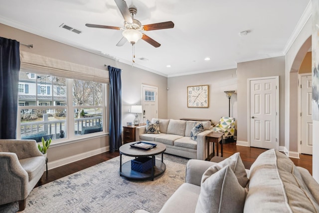 living area with baseboards, visible vents, arched walkways, and crown molding