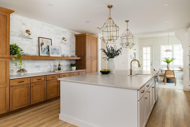 kitchen featuring hanging light fixtures, backsplash, light wood-style flooring, a sink, and an island with sink