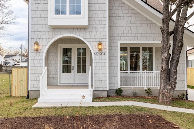 entrance to property featuring french doors, a porch, and fence