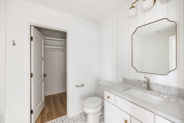 half bath featuring toilet, baseboards, wood finished floors, and vanity