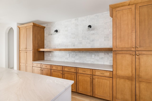 kitchen with light wood finished floors, arched walkways, brown cabinetry, open shelves, and backsplash