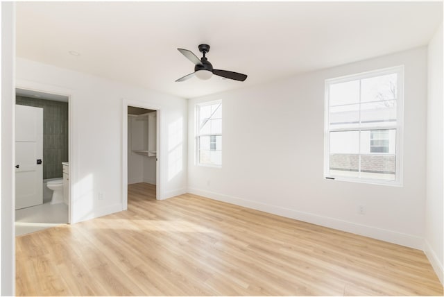 unfurnished bedroom with baseboards, light wood-style flooring, ensuite bathroom, a walk in closet, and a closet