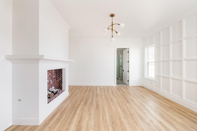 unfurnished living room with baseboards, crown molding, light wood-type flooring, a fireplace, and a chandelier