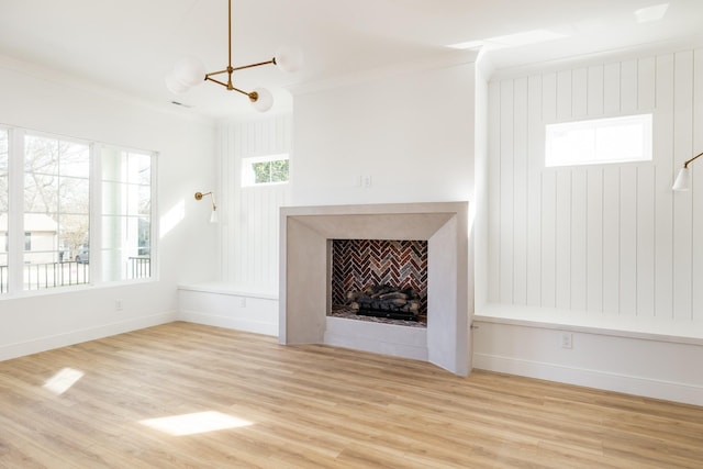 unfurnished living room with a chandelier, a fireplace, wood finished floors, baseboards, and ornamental molding