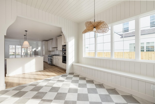 kitchen featuring decorative light fixtures, light floors, stainless steel appliances, a sink, and wall chimney exhaust hood