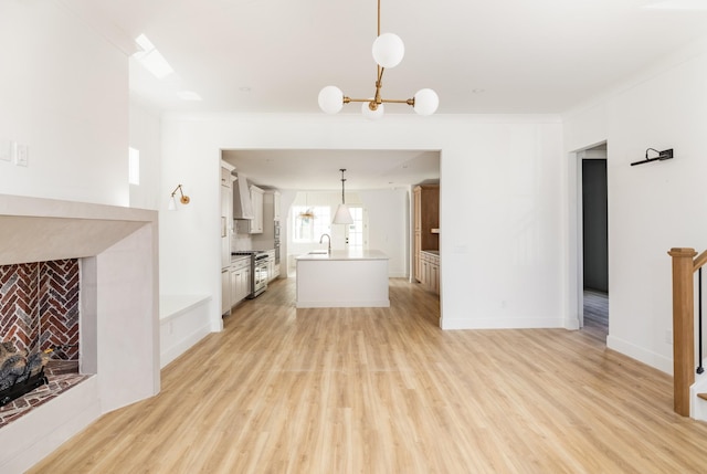 unfurnished living room featuring a fireplace, a sink, baseboards, light wood-style floors, and ornamental molding