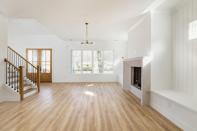 unfurnished living room featuring a notable chandelier, a fireplace, light wood-style flooring, baseboards, and stairs