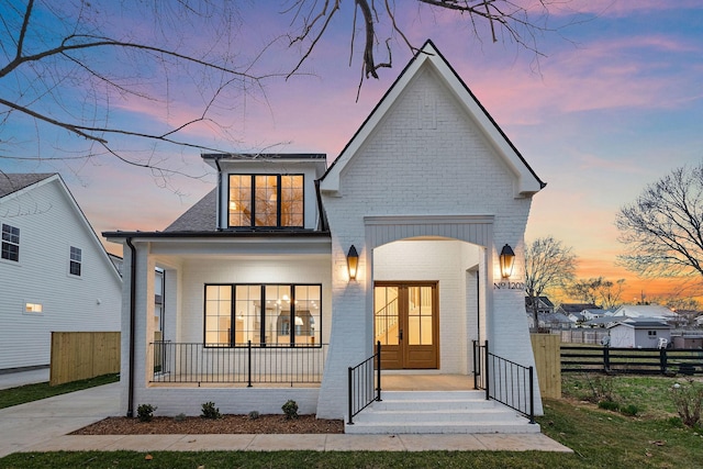 view of front facade with french doors, brick siding, roof with shingles, a porch, and fence