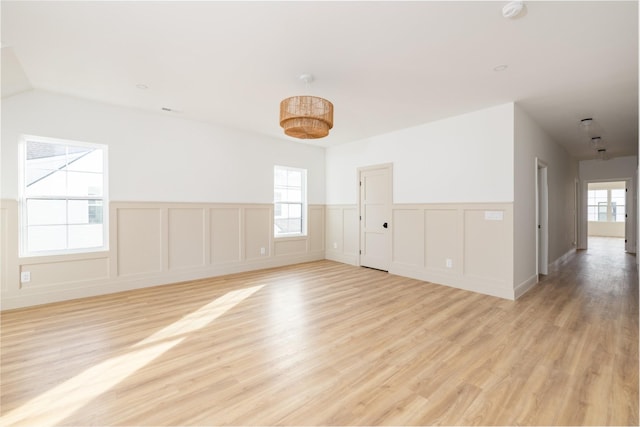 empty room featuring light wood-style floors, plenty of natural light, and wainscoting