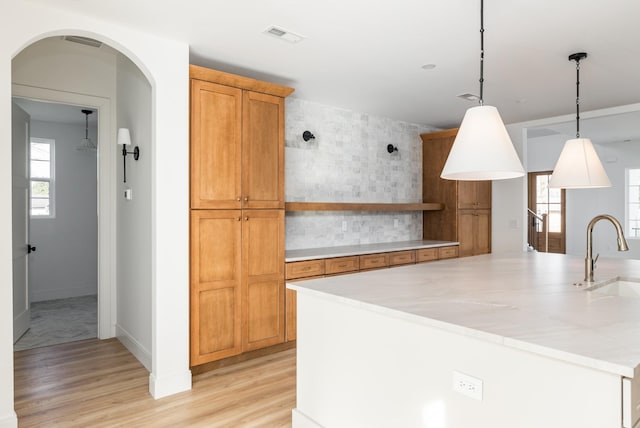 kitchen featuring a sink, light countertops, light wood-type flooring, decorative backsplash, and open shelves