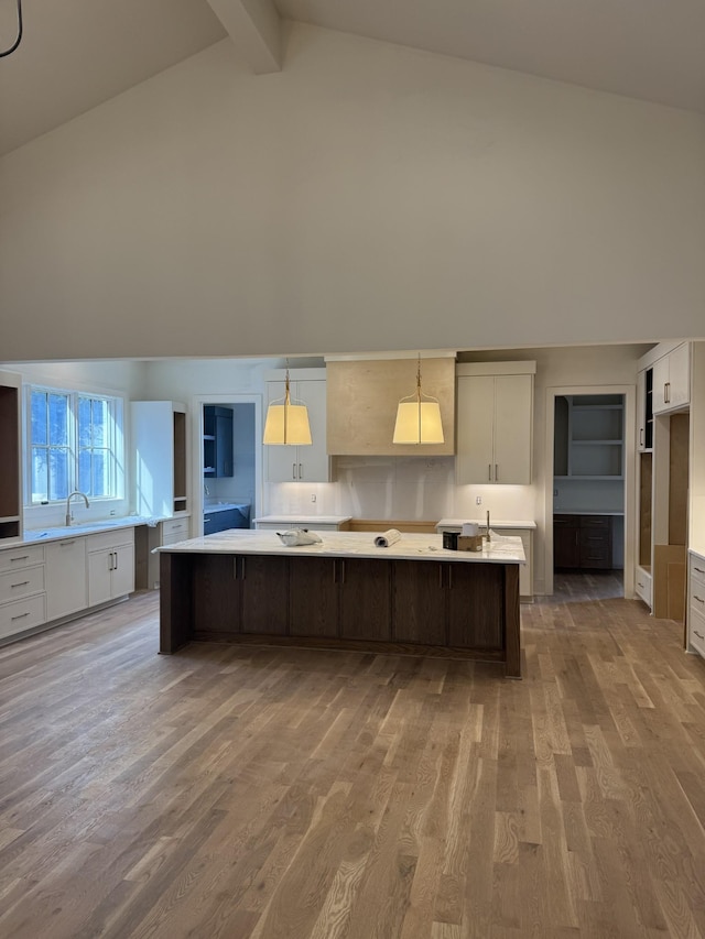 kitchen featuring light wood finished floors, light countertops, white cabinets, a sink, and high vaulted ceiling