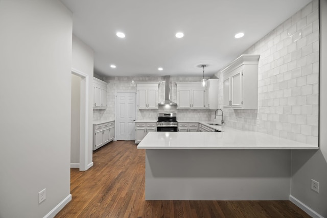 kitchen featuring electric range, decorative backsplash, wall chimney exhaust hood, a peninsula, and a sink