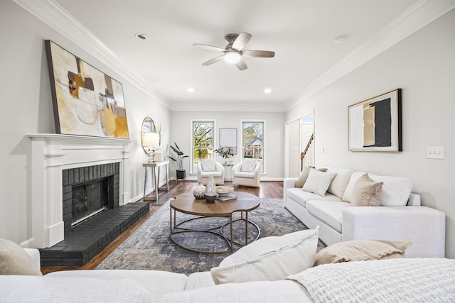 living room with wood finished floors, baseboards, ceiling fan, crown molding, and a brick fireplace