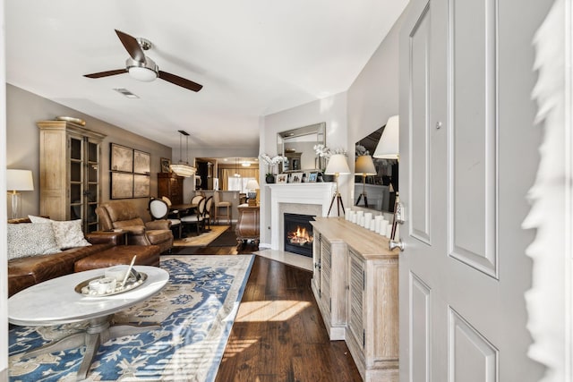 living area featuring dark wood-style floors, a fireplace with flush hearth, visible vents, and ceiling fan