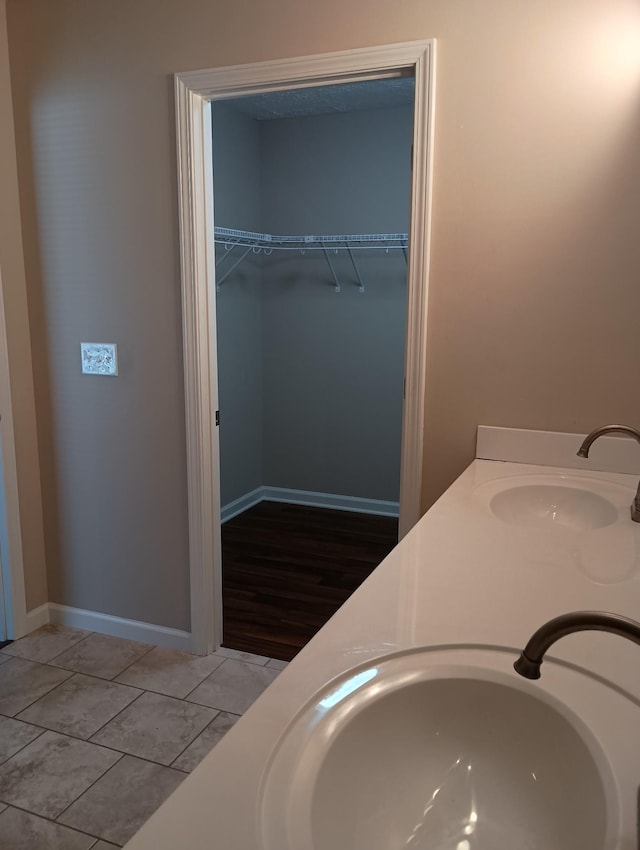 full bath featuring double vanity, baseboards, a walk in closet, and a sink