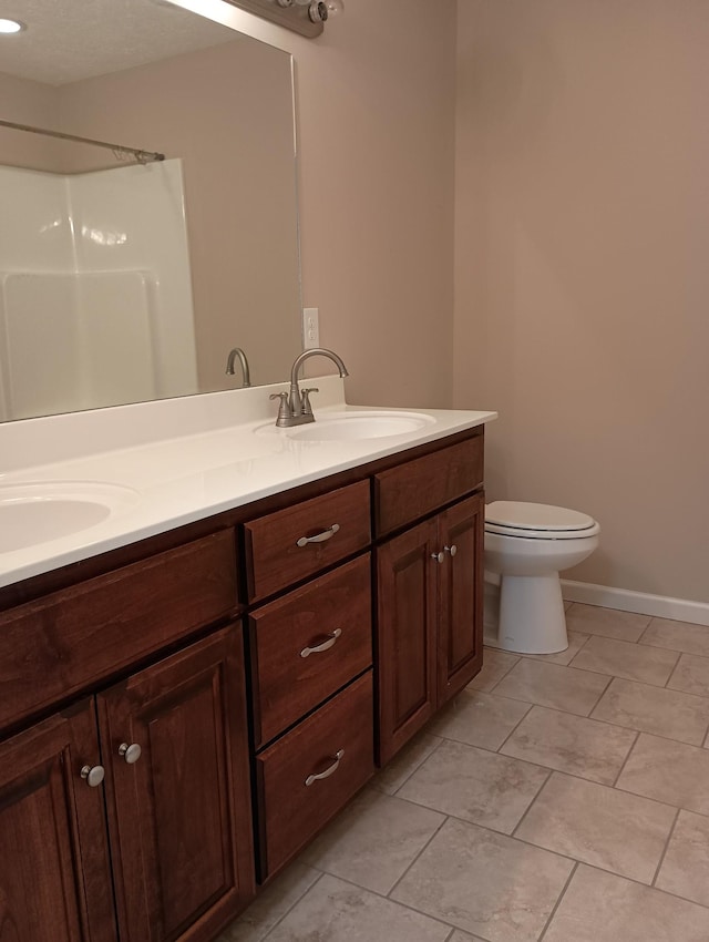 full bathroom with toilet, a sink, baseboards, double vanity, and walk in shower