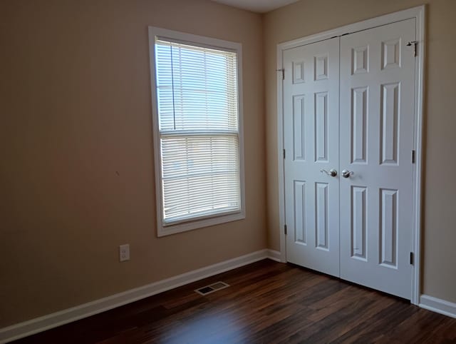 unfurnished bedroom featuring a closet, dark wood-style flooring, visible vents, and baseboards