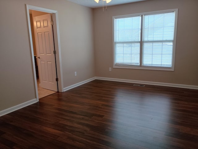 empty room featuring dark wood-type flooring, visible vents, ceiling fan, and baseboards