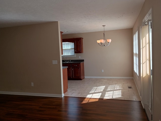 unfurnished dining area with baseboards, visible vents, a textured ceiling, light wood-type flooring, and a chandelier