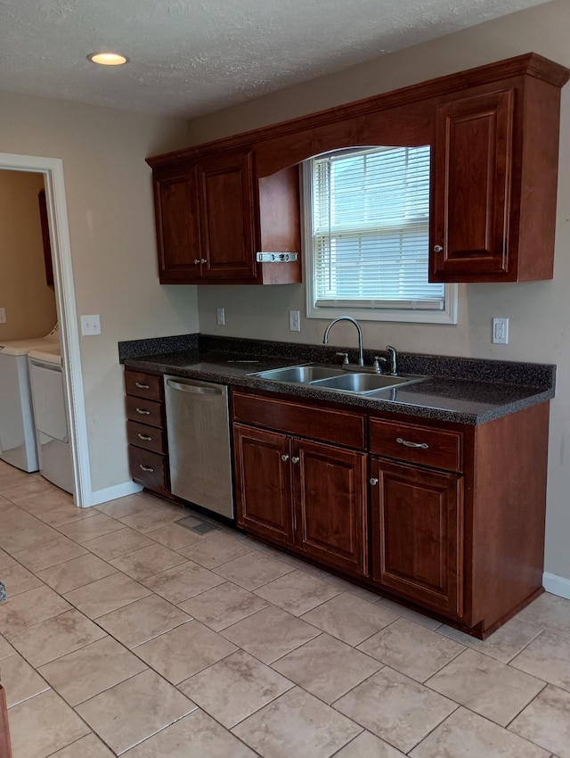 kitchen featuring a textured ceiling, a sink, stainless steel dishwasher, dark countertops, and washing machine and clothes dryer