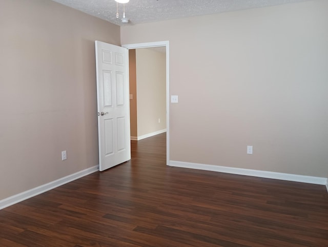 spare room featuring a ceiling fan, baseboards, dark wood finished floors, and a textured ceiling