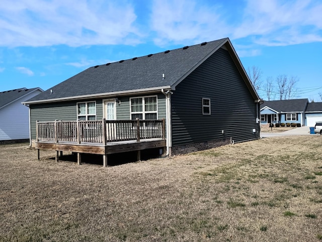 rear view of house featuring a shingled roof, a deck, and a lawn