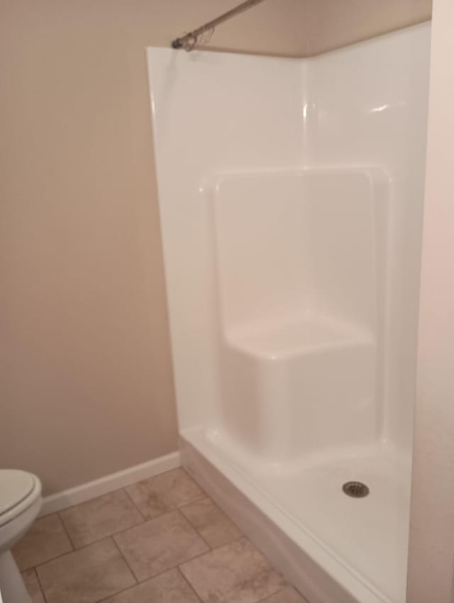 full bathroom featuring a shower, tile patterned floors, toilet, and baseboards